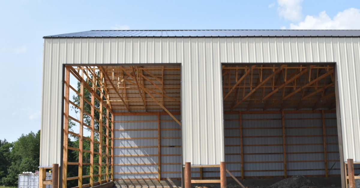 A post-frame building under construction with visible wood framing and partially installed metal siding.