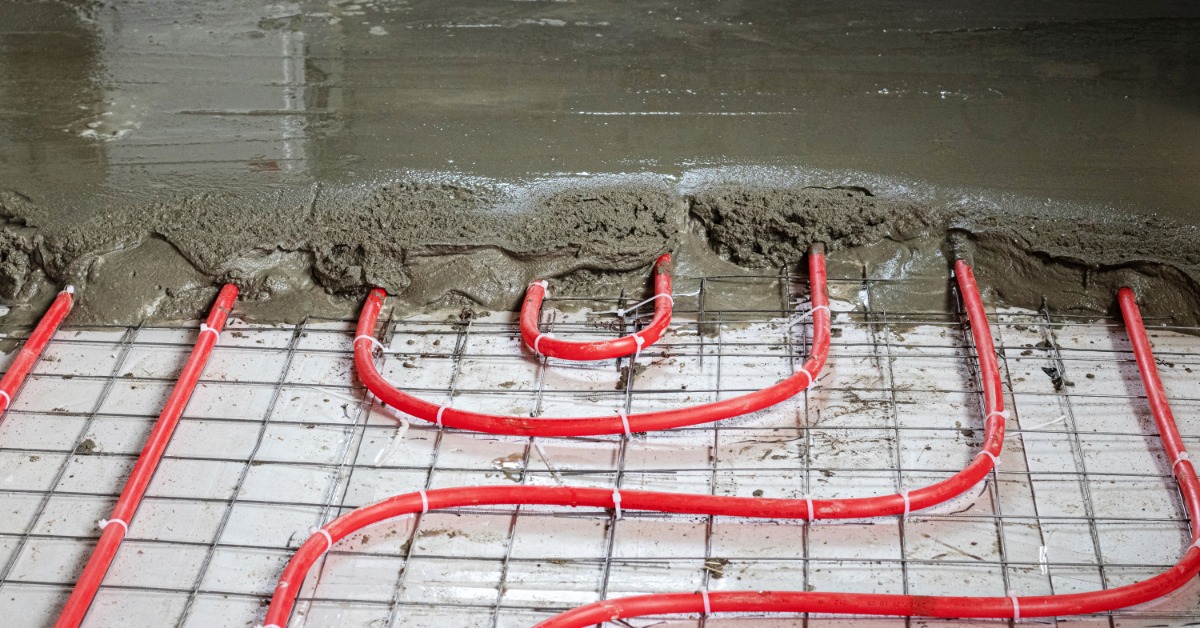 lesterbuildingsystems-470714-concrete-floors-heating-system-imageb.jpg Red radiant heating tubes run beneath a concrete floor as workers pour wet concrete over the heating system.