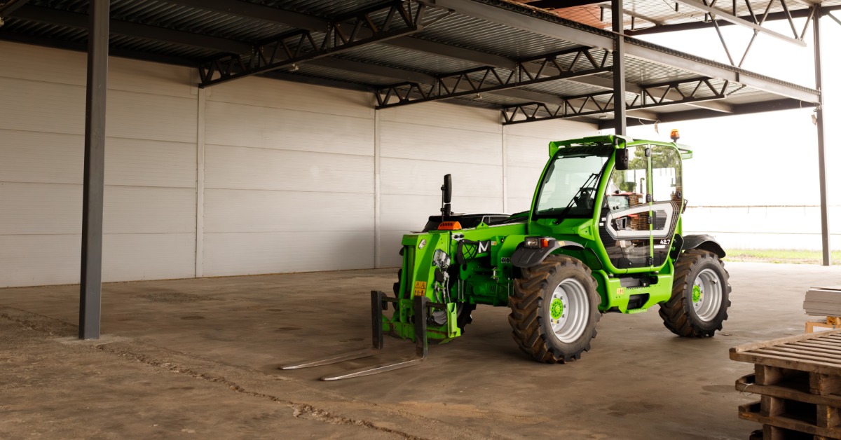 lesterbuildingsystems-470714-green-tractor-building-blogbanner-(1).jpg A green telehandler sits on a concrete floor inside a large agricultural building with an open equipment storage area.