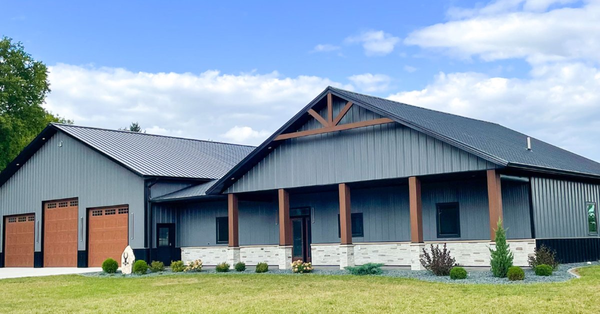 Lester-Building-Systems-LLC-439188-ImageB.jpg A gray metal building with a blue roof, wood posts, orange doors, grass, shrubs, and trees in the background.