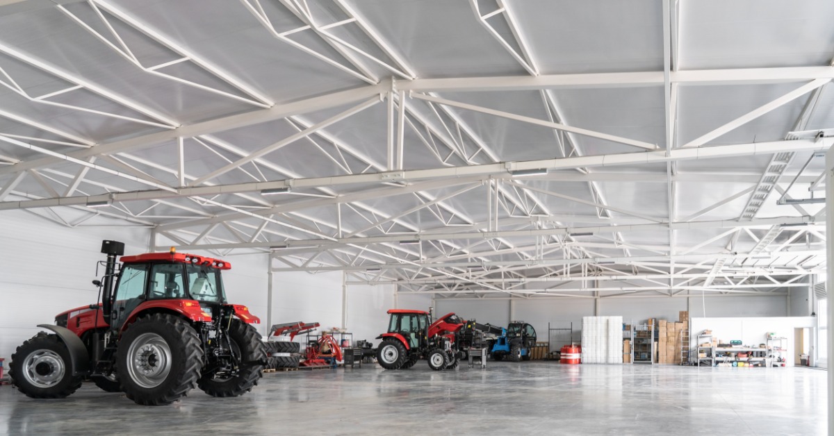 lesterbuildingsystems-470700-farm-machinery-facility-imageb.jpg Several tractors and farm machines sit inside a spacious shop with open floor space for equipment movement.